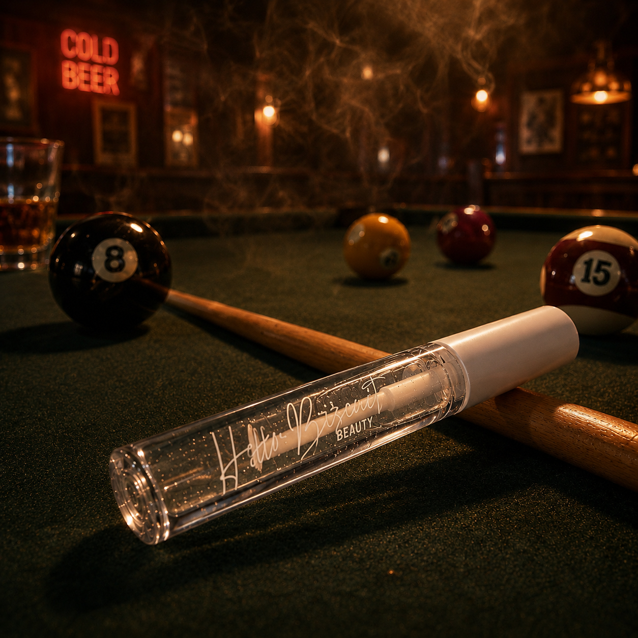 A clear tube of Hello Biscuit Beauty Cowboy Casanova Clear Lip Gloss resting on a green felt pool table next to a pool cue and billiard balls in a moody western bar setting