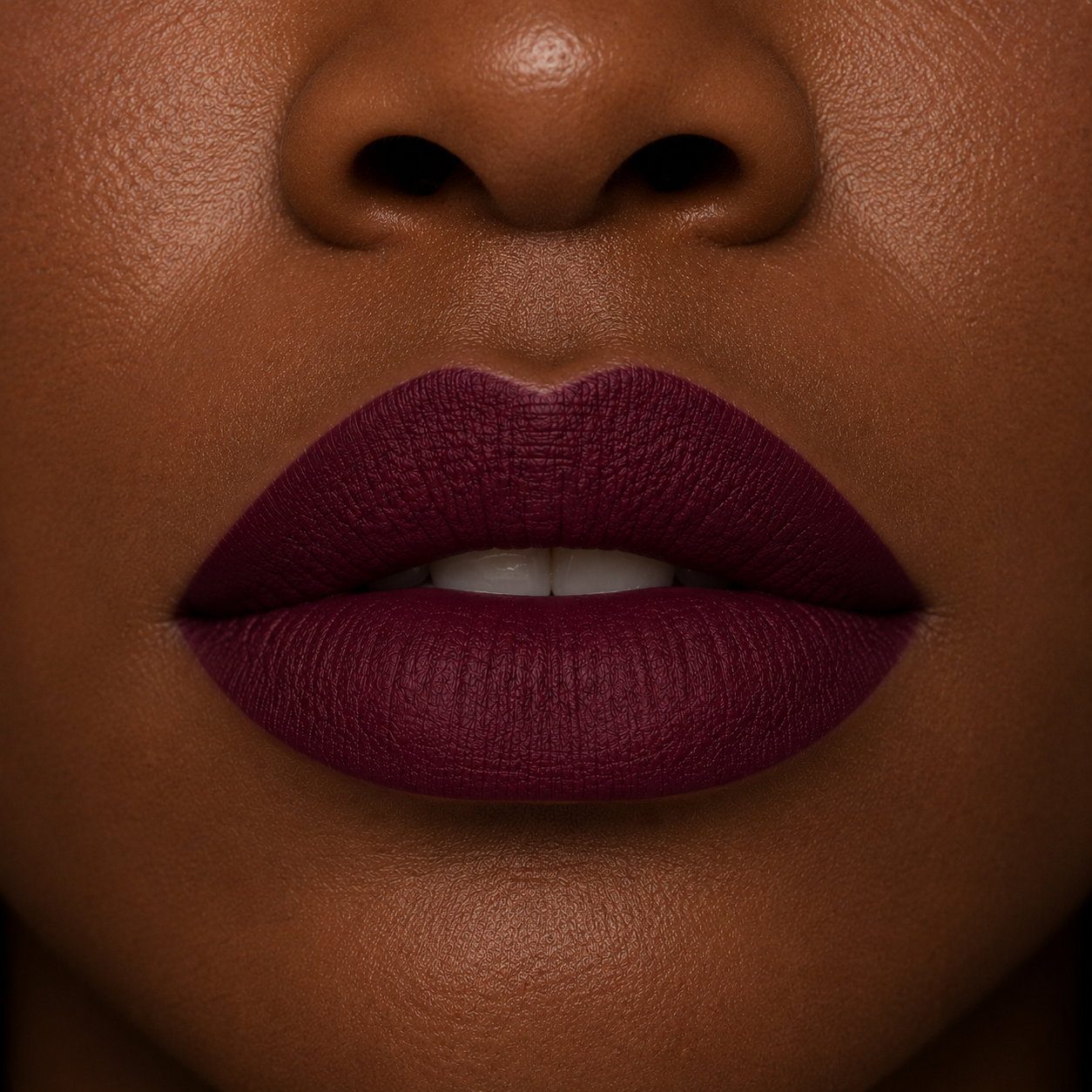 A detailed close up view of full lips on a deep skin tone wearing Hello Biscuit Beauty Jolene matte lipstick, a deep sparkling burgundy red wine shade with a smooth velvet matte finish