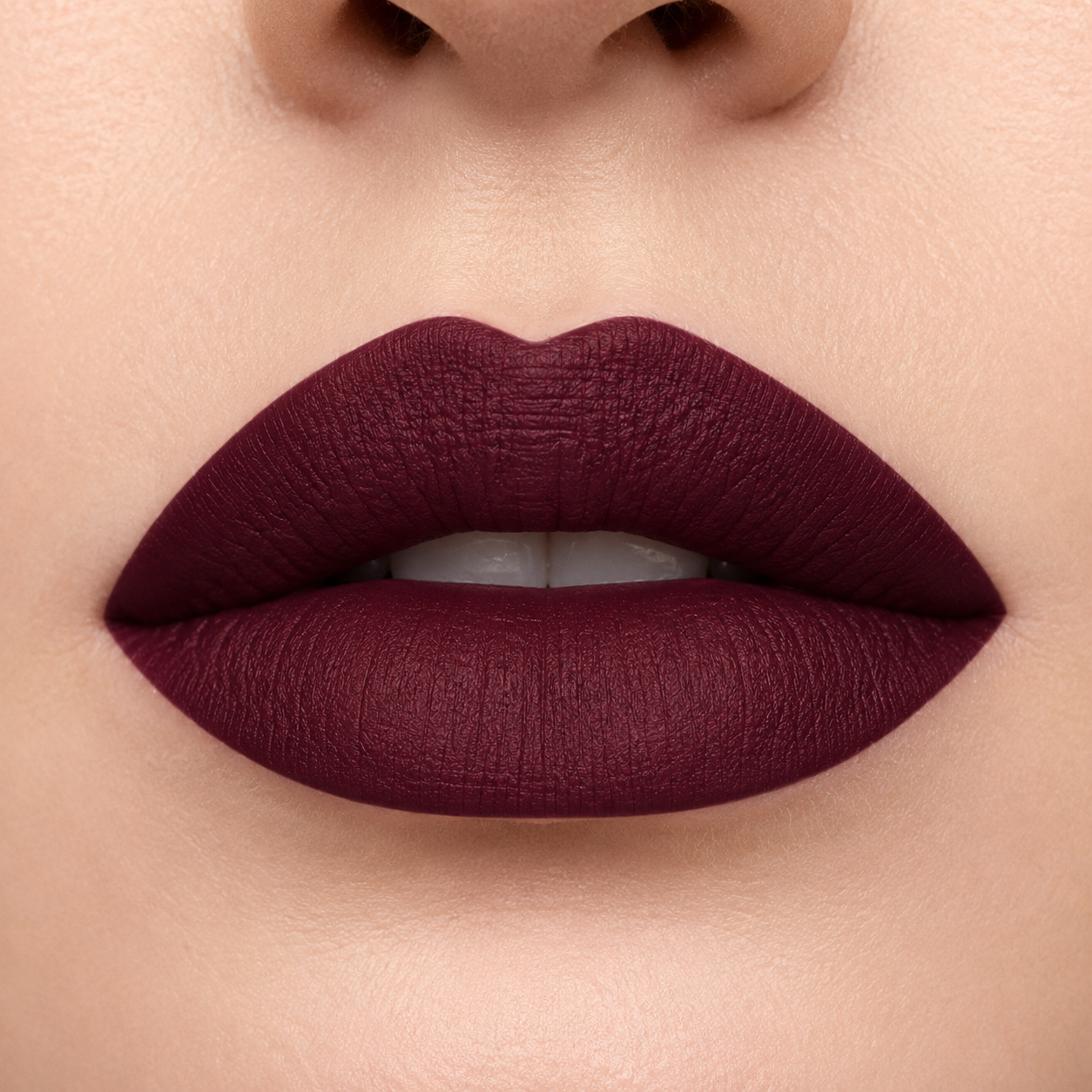 A detailed close up view of full lips wearing Hello Biscuit Beauty Jolene matte lipstick, a deep sparkling burgundy red wine shade with a smooth velvet matte finish