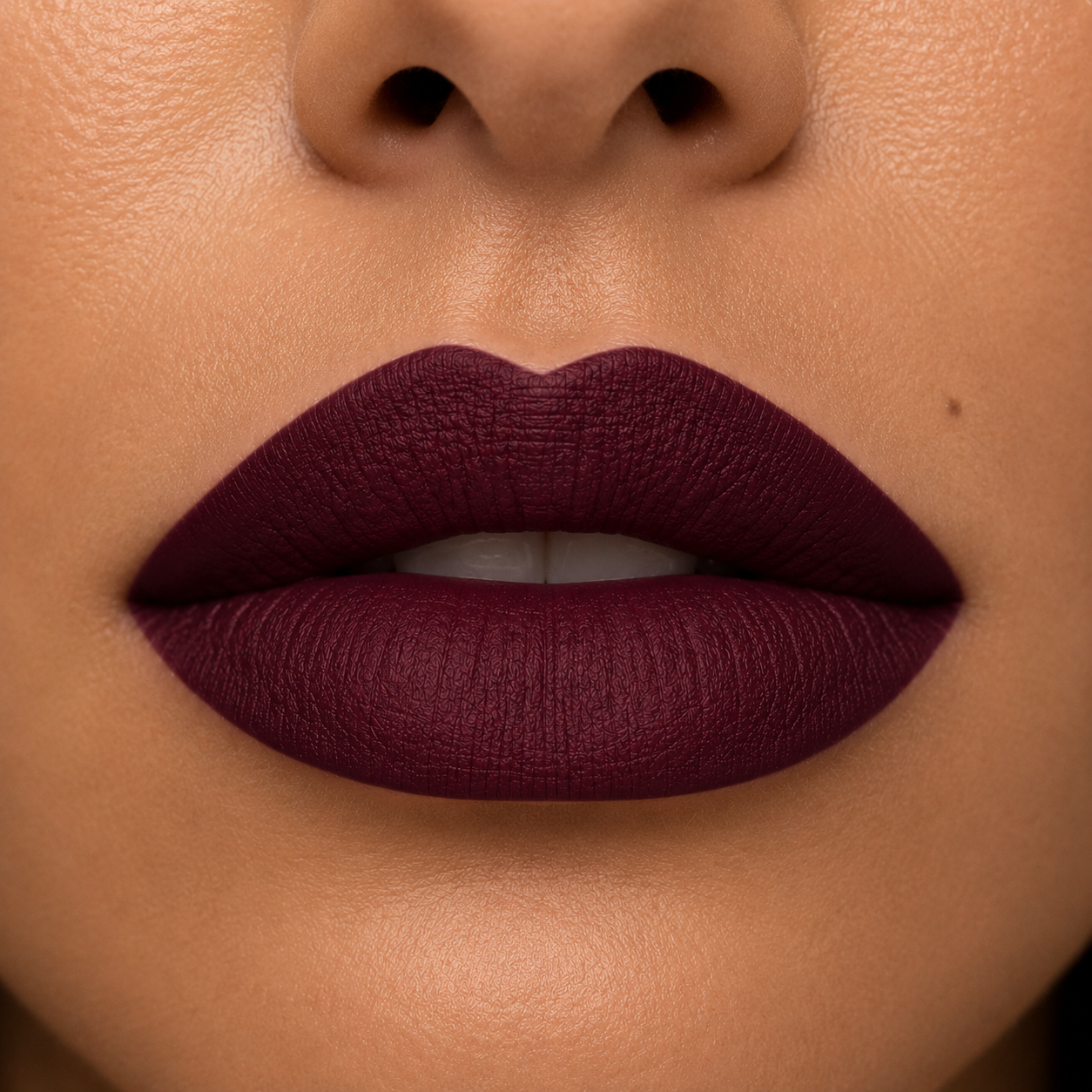 A detailed close up view of full lips on a warm skin tone wearing Hello Biscuit Beauty Jolene matte lipstick, a deep sparkling burgundy red wine shade with a smooth velvet matte finish