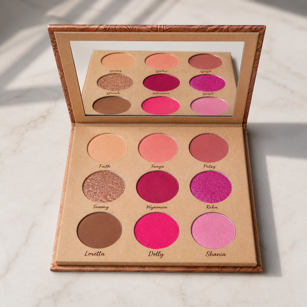 An open Hello Biscuit Beauty Queens of Country Eye Shadow Palette on a marble surface showcasing nine matte and shimmer eyeshadow shades and a built-in mirror
