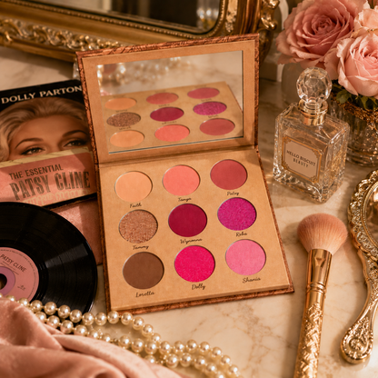 An open Hello Biscuit Beauty Queens of Country Eye Shadow Palette displayed on a vanity next to a crystal perfume bottle a makeup brush pink roses and vintage Patsy Cline and Dolly Parton vinyl records