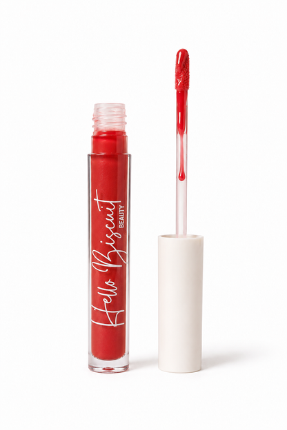 An open clear tube of Hello Biscuit Beauty Two Dozen Roses lip gloss standing upright with the white cap off and the doe foot applicator wand pulled out to show the vibrant true red glossy formula