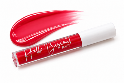 A tube of Hello Biscuit Beauty Two Dozen Roses lip gloss standing in front of a thick high shine swipe of the vibrant true red shade on a clean white background